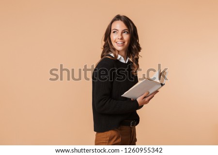 Photo of gorgeous woman 20s holding book while looking back isolated over beige background