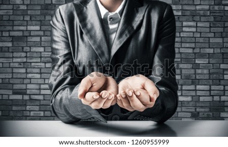 Cropped image of businessman in black suit presenting empty palms with gray brick wall on background. 3D rendering.