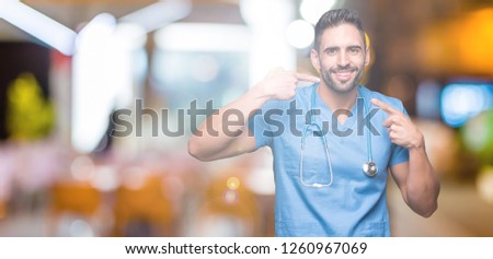 Handsome young doctor surgeon man over isolated background smiling confident showing and pointing with fingers teeth and mouth. Health concept.