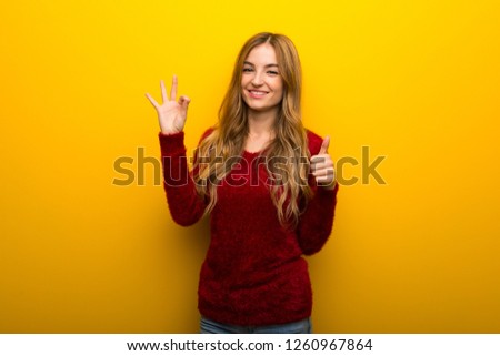 Young girl on vibrant yellow background showing ok sign with and giving a thumb up gesture