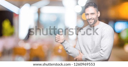 Young handsome man wearing sweatshirt over isolated background Looking proud, smiling doing thumbs up gesture to the side