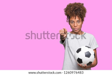 Young african american woman holding soccer football ball over isolated background pointing with finger to the camera and to you, hand sign, positive and confident gesture from the front