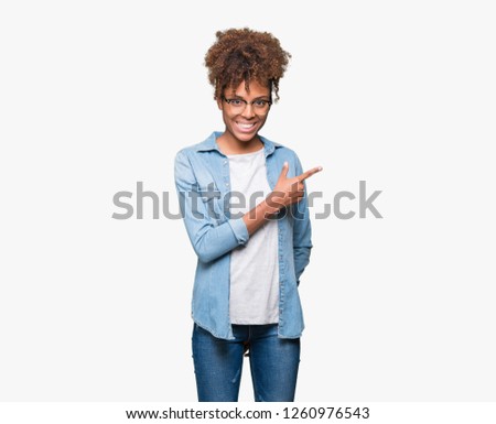 Beautiful young african american woman wearing glasses over isolated background cheerful with a smile of face pointing with hand and finger up to the side with happy and natural expression on face