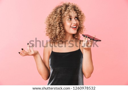 Portrait of caucasian curly woman 20s smiling and talking on mobile phone isolated over pink background