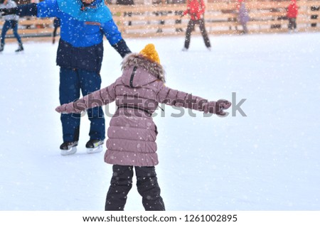 Rink. Father and daughter on a skating rink. Dad trains little daughter to skate on ice. Winter sports.