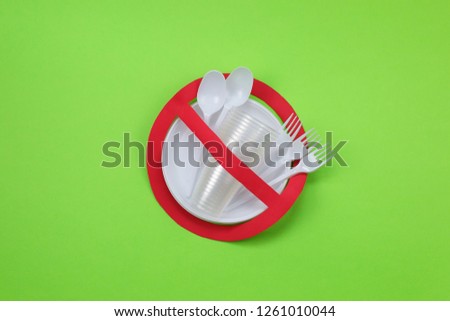 No use symbol in red forbidden sign with plastic dishes on green background. Environmental concept. Ban single use plastic.