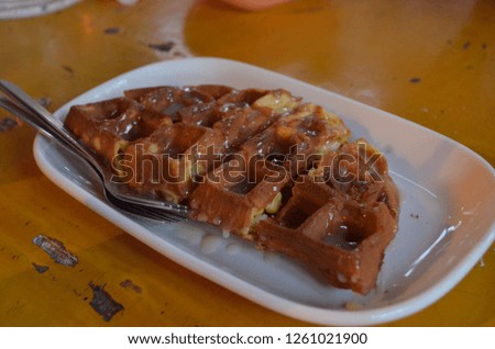 Homemade waffle with corn, coconut and raisin filling, top with concentrated milk served in a white plate on a yellow table for refreshment