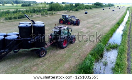 Aerial picture of two tractors work together collecting plastic wrapped bales with silage is fermented high-moisture stored fodder which can be fed to cattle sheep and other such ruminants