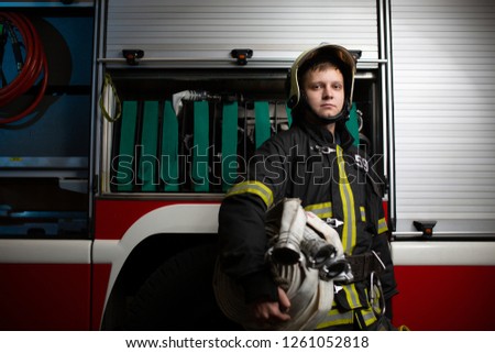 Image of firefighter with hoses in hands on background of fire truck