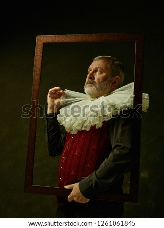 Official portrait of historical governor from the golden age with corrugated round collar and a man with an empty picture frame . Studio shot against dark wall.