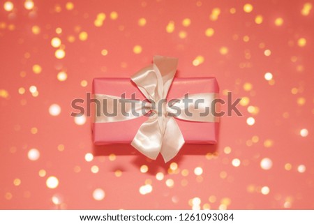 Festive picture with lightening golden bokeh lights. Pink gift with satin bow on coral background. Christmas. Wedding. Birthday. Happy woman's day. Mothers Day. Valentine's Day. Flat lay.