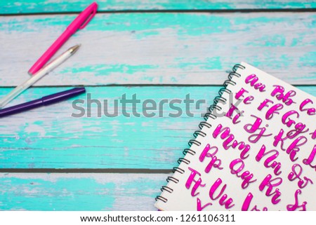 Close up of notebook with hand drawn abc alphabet letters and colorful pens on blue wooden desk background. Back to school concept