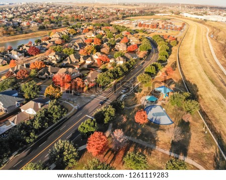 Top view row of single-family houses sandwiches between community lake and public park with basketball court and pathway. Beautiful early autumn morning with colorful leaves near Dallas, Texas