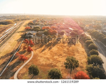 Aerial view residential neighborhood near public park with pathway and beautiful autumn trees. Row of single-family houses near small creek