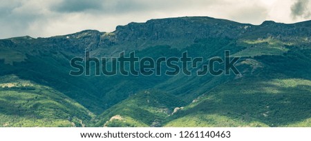 Panoramic natural scenery. Beautiful mountain landscape with light and dark green forest in the foothills, peaks, dramatic gray white clouds in sky. Central Balkan mountains, Stara planina, Bulgaria.