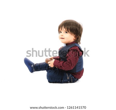Adorable young boy sitting on the floor while holding a chocolate doughnut against a white background