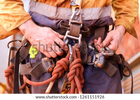 Closeup picture of male rope access worker hand wearing full safety harness clipping Karabiner on a chair into harness loop prior to abseiling working at height construction site, Sydney, Australia