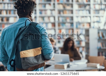 Waist up of Afro-American young man in casual clothes having backpack on one shoulder while coming to the university library