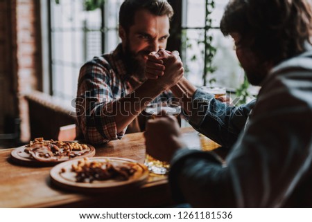 Friends having arm-wrestling match while sitting at the table with beer and snacks. Focus on male hands