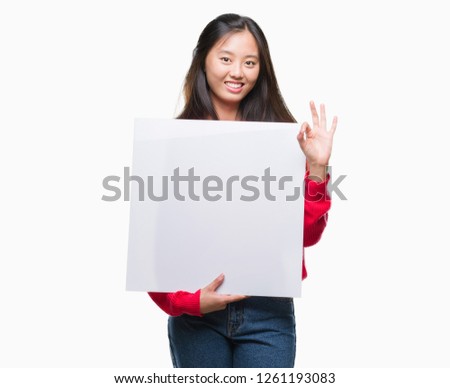 Young asian woman holding banner over isolated background doing ok sign with fingers, excellent symbol