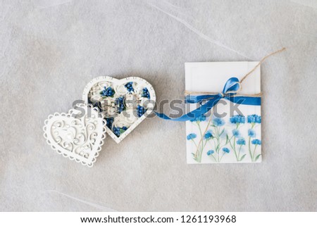gold wedding rings in a heart shaped ring box with white and blue flowers and a wedding invitation with cornflowers
