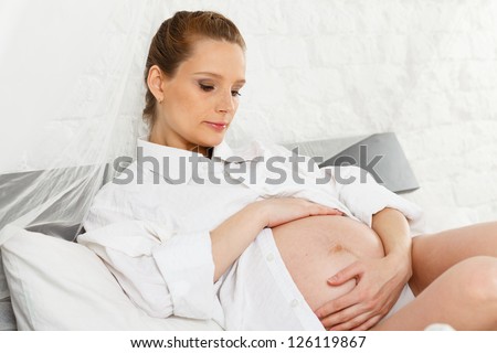 Pregnant woman lies on the house bed.