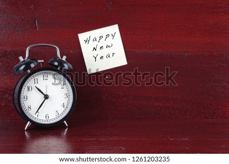"Happy New Year" wording on a stick note with alarm clock on the wooden table