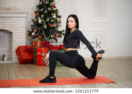Young sport woman doing stretching exercise near Christmas tree and gift boxes
