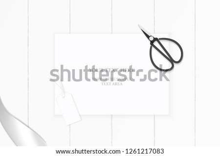 Flat lay top view elegant white composition paper silver ribbon tag and vintage metal scissors on wooden background.