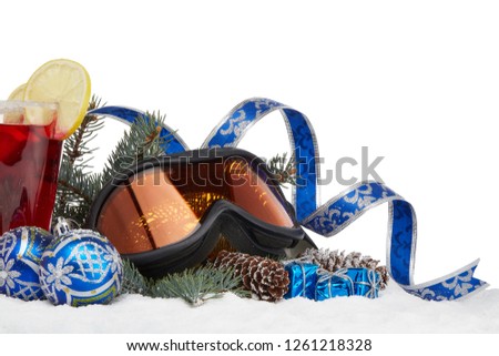 Winter holidays still life with fir tree branch, ski glasses, fruit tea and Christmas decorations lying on snow on a white background with copy space. New Year and Christmas. Winter vacation.