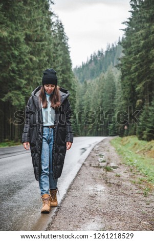 woman at the middle of the road in mountain forest. road trip