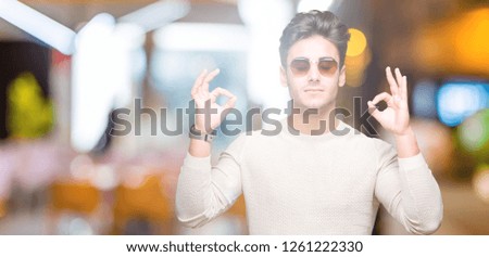 Young handsome man wearing sunglasses over isolated background relax and smiling with eyes closed doing meditation gesture with fingers. Yoga concept.
