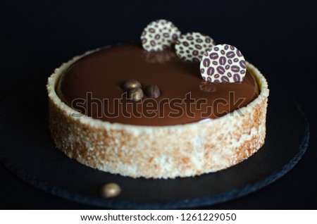 Chocolate coffee mousse cake covered with chocolate glaze and decorated with chocolate elements on black background