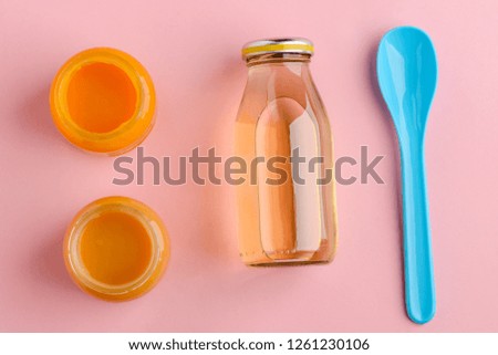 Jars of baby food, bottle of juice and blue spoon on pink background. Feeding child on the go.