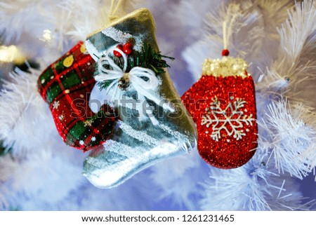 Red Christmas boot with a red mitten on the background of a white Christmas tree, the theme of decorative toys and Christmas
