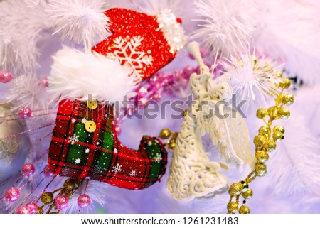Red Christmas boot with a white angel and red mitten on the background of a white Christmas tree, the theme of decorative toys and Christmas

