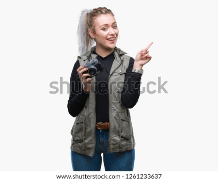 Young blonde woman taking pictures using vintage camera over isolated background very happy pointing with hand and finger to the side