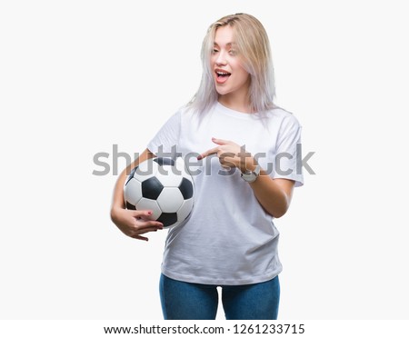 Young blonde woman holding soccer football ball over isolated background very happy pointing with hand and finger
