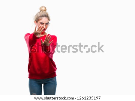 Young beautiful blonde woman wearing red sweater and glasses over isolated background afraid and terrified with fear expression stop gesture with hands, shouting in shock. Panic concept.