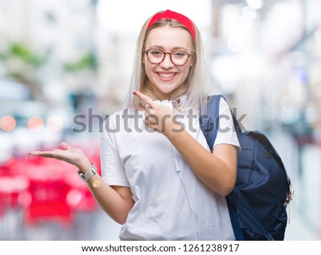 Young blonde student woman wearing glasses and backpack over isolated background amazed and smiling to the camera while presenting with hand and pointing with finger.