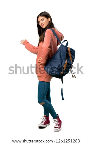A full-length shot of a Teenager girl with sweatshirt and backpack pointing back and presenting a product