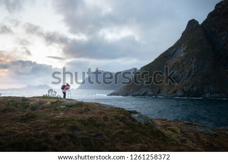 Landscape : woman is taking a photo with the camera and tripod at the fjord in Lofoten Norway