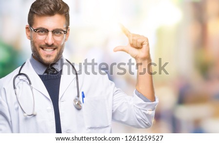 Young handsome doctor man over isolated background smiling and confident gesturing with hand doing size sign with fingers while looking and the camera. Measure concept.