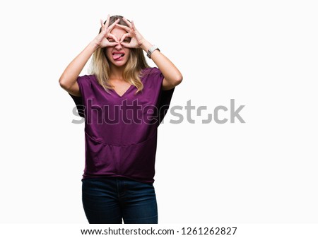 Young beautiful blonde elegant woman over isolated background doing ok gesture like binoculars sticking tongue out, eyes looking through fingers. Crazy expression.