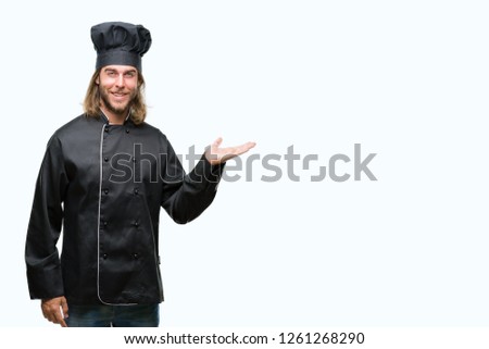 Young handsome cook man with long hair over isolated background smiling cheerful presenting and pointing with palm of hand looking at the camera.