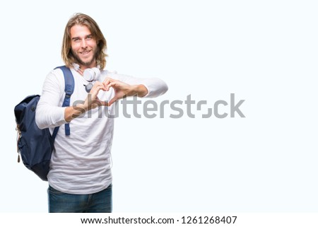 Young handsome tourist man with long hair wearing backpack over isolated background smiling in love showing heart symbol and shape with hands. Romantic concept.