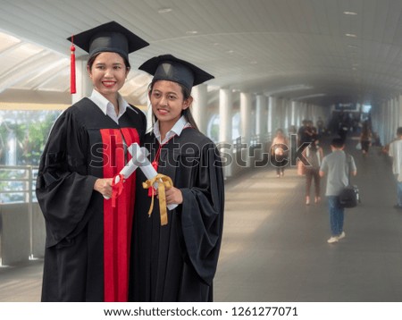 Two young ladies smiling with certificate in hands after graduation ceremony with long path as background.  
