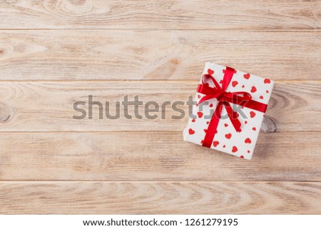 Valentine or other holiday handmade present in paper with red hearts and gifts box in holiday wrapper. Present box of gift on orange wooden table top view with copy space, empty space for design.