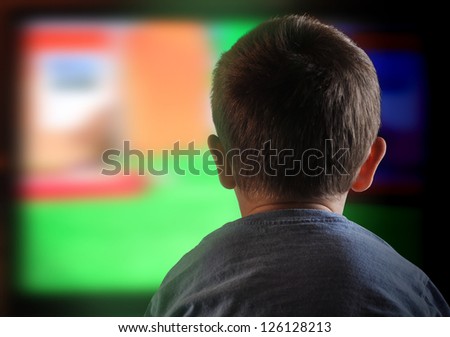 A young boy is watching a television screen with his back for a tv effect on children or a communication concept.