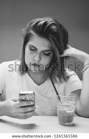 beautiful black and white photo of Caucasian young female with dark hair,sitting in cove,drinking coffee and looking at her phone